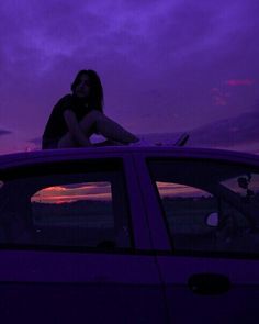 a woman sitting on top of a car in the dark at night with purple clouds