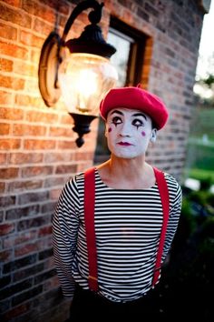 a man wearing a clown mask and suspenders standing in front of a brick wall