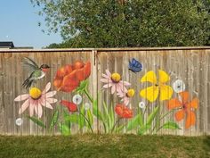 a wooden fence with flowers painted on it and a hummingbird flying over the top