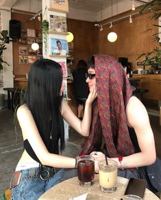 two women sitting at a table with drinks in front of them and one woman covering her face