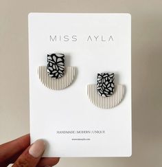 a pair of black and white earrings is shown in front of a card that says miss alya