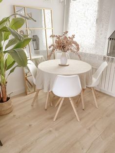 a dining room table with white chairs and a potted plant in the corner next to it