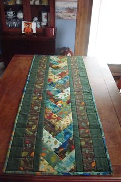 a wooden table topped with a green and multi colored quilted table runner on top of a wooden dining room table