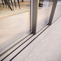 an open glass door on the outside of a building with chairs and tables in the background