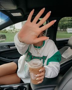 a woman holding her hand up in the back seat of a car with a cup of coffee