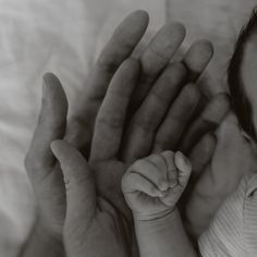 a black and white photo of a baby holding its hand up to the camera,