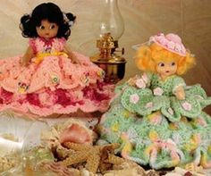 two little dolls sitting next to each other on a table with shells and seashells