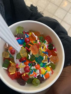 a white bowl filled with gummy bears on top of a counter next to a persons hand