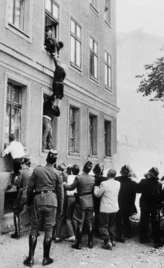 an old black and white photo of men hanging from the side of a tall building