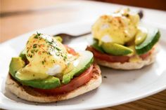 two open faced sandwiches topped with avocado and tomato on a white plate next to a fork