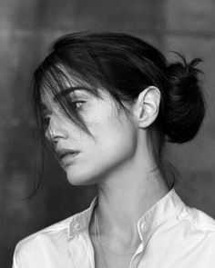 a black and white photo of a woman with her hair in a high bun, looking to the side