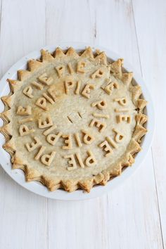 a pie with letters written on it sitting on top of a white plate next to a knife and fork