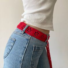 a woman is wearing a red belt with crochet lace on it and has her back to the camera