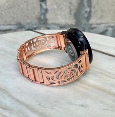 Floral Rose Gold Band With Heart Charm Compatible with: Galaxy Watch 7 | Galaxy Watch 6 | Galaxy Watch 5 | Galaxy Watch 4  Includes Extra Links and Pins Tool to Resize Wristband To Preferred Fitment Adjustable Size Fits 5.5 to 8 Inches (need to add or remove extra links) Super Light Bracelet - Weighs Around 1.2 oz  18mm  Wide Designed And Handmade by Simeon D Jewelry  This Product Is Not Water Resistant/Proof And Not Suitable for Workouts Not For Other Models. Samsung Galaxy Watch Is NOT Include Rose Gold Stainless Steel Watch Bands For Gift, Rose Gold Stainless Steel Watch Band As Gift, Rose Gold Round Stainless Steel Watch Accessories, Rose Gold Bracelet Strap Watch Accessories, Rose Gold Round Bracelet Strap Watch Accessories, Rose Gold Round Watch With Bracelet Strap, Rose Gold Watch Bands As Gift, Galaxy Watch 5 Pro, Galaxy Watch 5