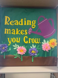 a sign that reads reading makes you grow with flowers and watering can in the background