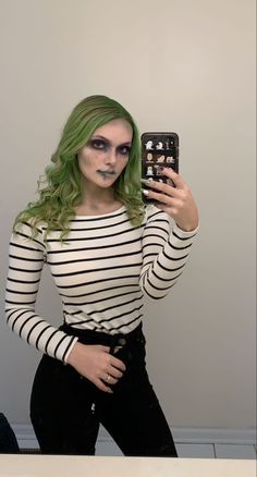 a woman with green hair and makeup taking a selfie in front of a mirror