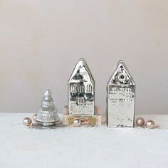 three small silver houses sitting next to each other on a white tablecloth covered surface