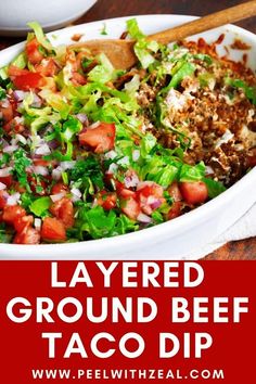 layered ground beef taco dip with lettuce and tomatoes in a white bowl