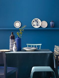 a dining room with blue walls and white plates on the wall, two chairs in front of a table