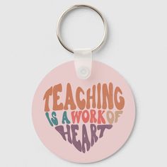 a pink keychain with the words teaching is a work of heart on it