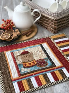 a quilted placemat with a teapot on it next to some cookies and oranges