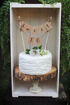 a white cake sitting on top of a wooden table next to a tree stump and greenery