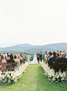 an outdoor wedding ceremony in the mountains with white flowers and greenery on the aisle