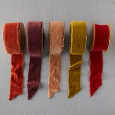 five different colored velvet ribbons hanging on a white wall with one red, one yellow and one brown