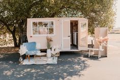 a small pink trailer parked in front of a tree with chairs and tables around it