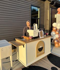 a woman standing behind a counter in front of a building with balloons on the outside