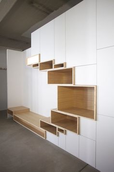 an empty room with white walls and wooden shelves on the wall, next to a bench