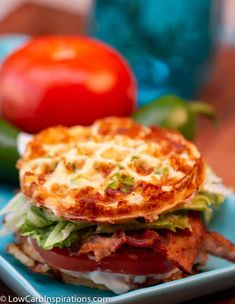 a bacon, lettuce and tomato sandwich on a blue plate with tomatoes in the background