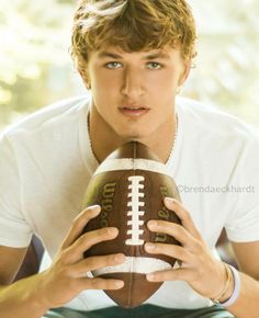 a young man is holding a football in his right hand and posing for the camera