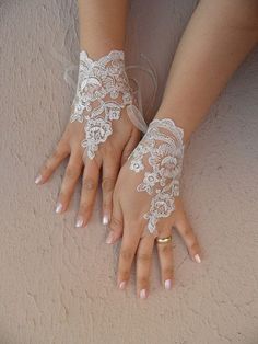 two hands with white lace on them, one holding the other's hand and wearing gold rings