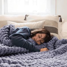 a woman laying in bed under a blue blanket