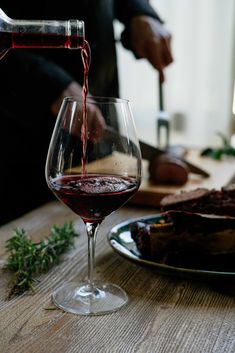 someone pouring red wine into a glass on a table