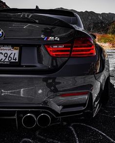 the back end of a bmw car parked in a parking lot with mountains in the background