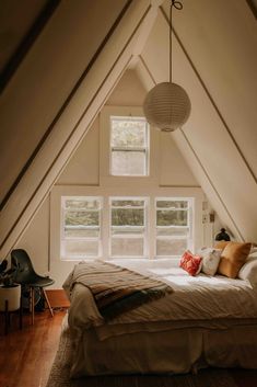 an attic bedroom with white walls and wood flooring is furnished with natural light from the windows