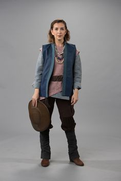 a woman standing in front of a gray background with a hat on her head and jacket over her shoulders