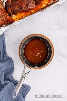 barbecue ribs and sauce in a cast iron skillet on a marble countertop next to a blue towel