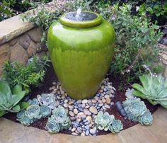 a green vase sitting in the middle of a garden filled with succulents