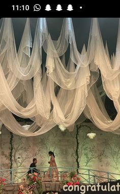 the bride and groom are standing under white draping in front of flowers on display