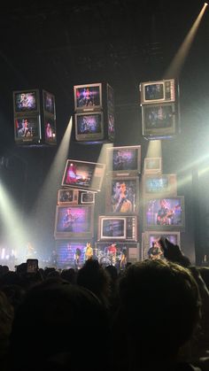 a group of people standing on top of a stage with lots of tv screens above them