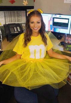 a woman wearing a yellow tutu sitting in front of a computer desk with her hands on her hips