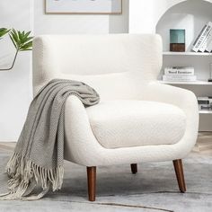 a white chair with a blanket on it in front of a book shelf and books