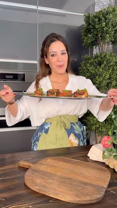 a woman holding a plate with food on it in front of an oven and cutting board