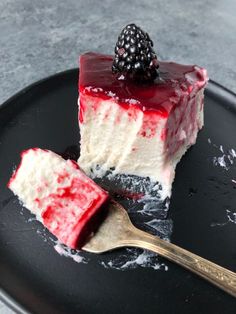 a piece of cheesecake with raspberry topping on a black plate next to a spoon