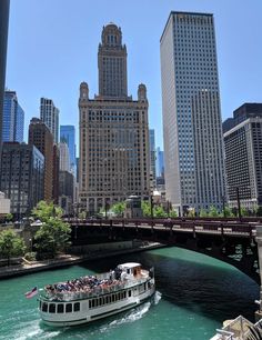 a boat is going down the river in front of some tall buildings and bridge with people on it