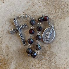 This one-decade rosary tenner in honor of St. Florian. The total length is 9 inches. This makes a unique and thoughtful gift to treasure. *Feast Day: May 4 *Patronage: Poland and Firemen Beads: I used larger English-cut glass beads in burgundy/greenfor the ten Hail Marys and one clear glass bead for the single Our Father.  Medals: The Crucifix is 1 1/2 inches and the saint medal is 1 inch. Both medals were made of base metal in Italy. *Free Gift Packaging: This rosary comes in a blue velour keepsake bag and gift box. *Care Tip: Over time, and with use, the medals may develop a patina. If you prefer to bring back the shine simply rub the medal with dampened baking soda and rinse with water. Faceted Beads Crucifix Rosary As Gift, Saint Florian, English Cut, St Florian, Decade Rosary, Our Father, Saints Medals, The Saint, Base Metal