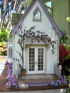 a small white house with purple flowers on the outside